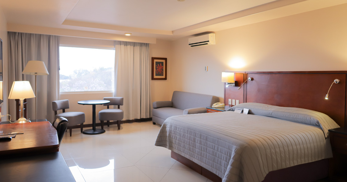 Modern guest room at Fortín Plaza Hotel Oaxaca with work desk, seating area, and natural light—ideal for MICE attendees seeking comfort and productivity during events.